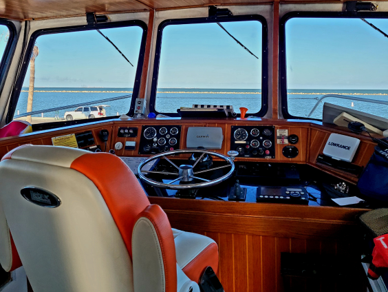 Texas Tease Boat cockpit with steering wheel and navigation equipment overlooking a calm blue sea under clear sky