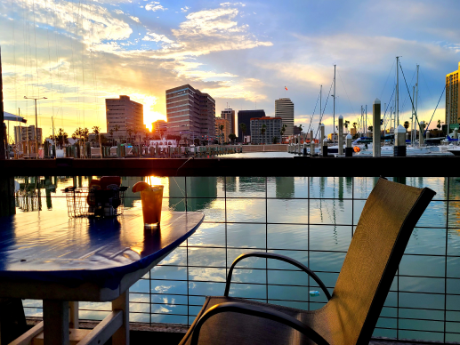 Sunset over marina with Corpus Christi skyline in background and empty chair and table in foreground